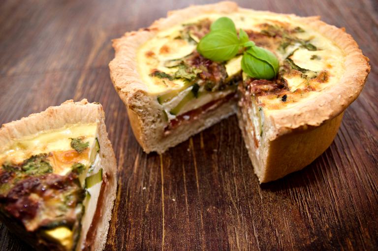 Un delicioso quiche mediterráneo de capas profundas con guarnición de albahaca.